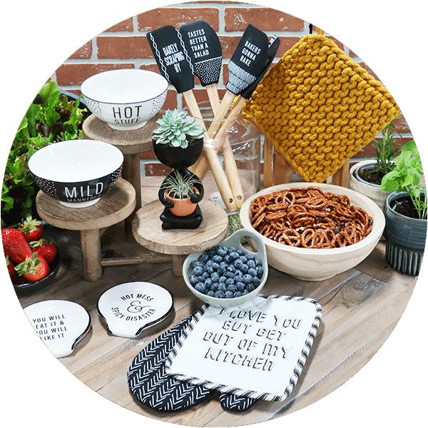 A collection of kitchen items with sayings on them, including spoon rests, oven mits, snack bowls, spatulas and berry bowls.